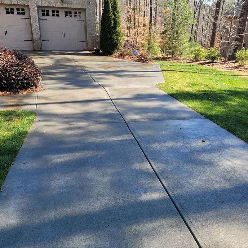 Concrete driveway leading to a two-car garage, bordered by grass and shrubbery.