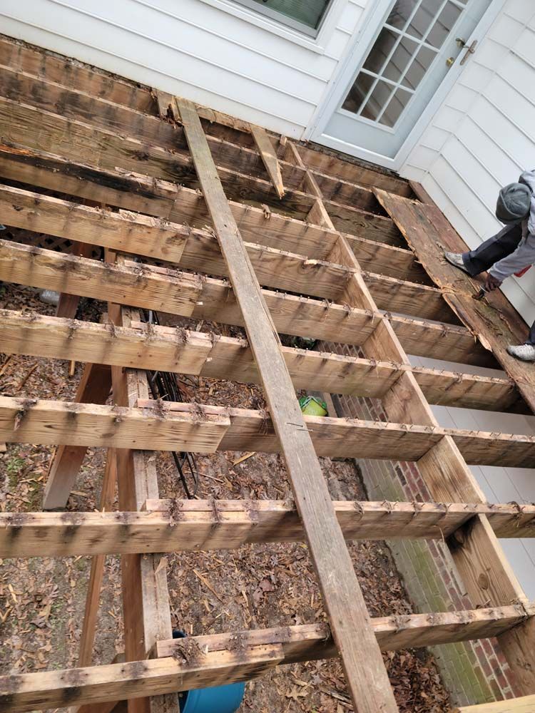 Overhead view of a deteriorated wooden deck frame. A person is standing to the right.