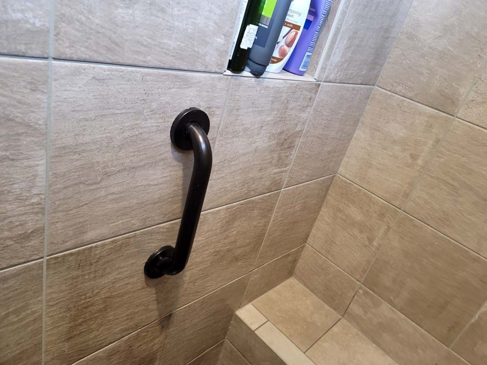 Dark, curved grab bar on beige tiled shower wall.