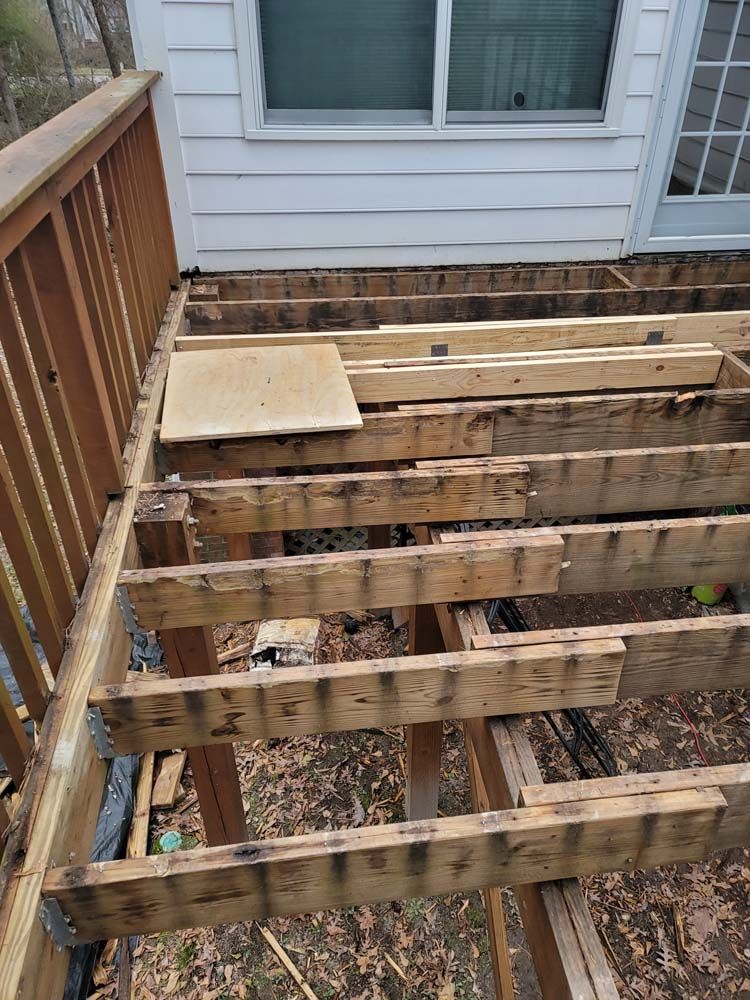Partially dismantled wooden deck with damaged boards.  Window and house siding are in the background.