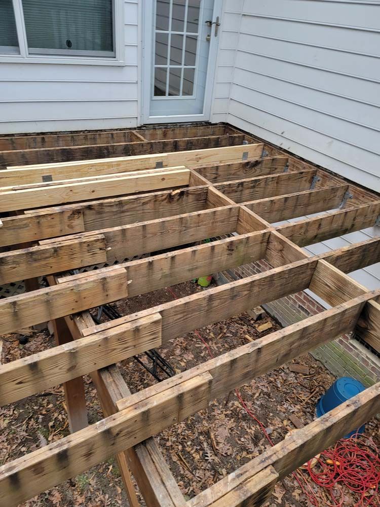 A partially disassembled wooden deck frame with a door and siding in the background.