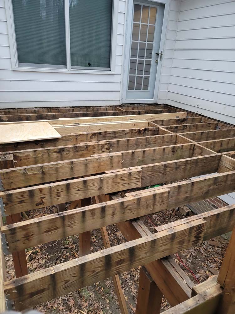 Partially disassembled wooden deck with exposed joists next to a house with a door.