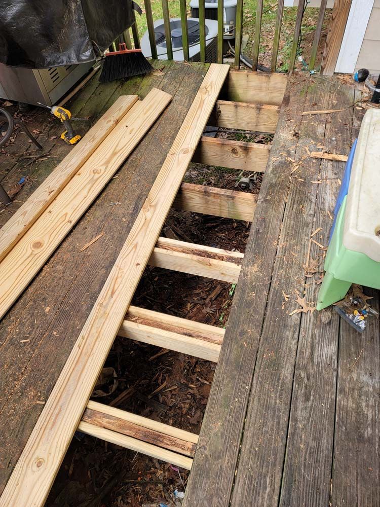 Deck repair: boards removed, revealing supports. New lumber nearby.