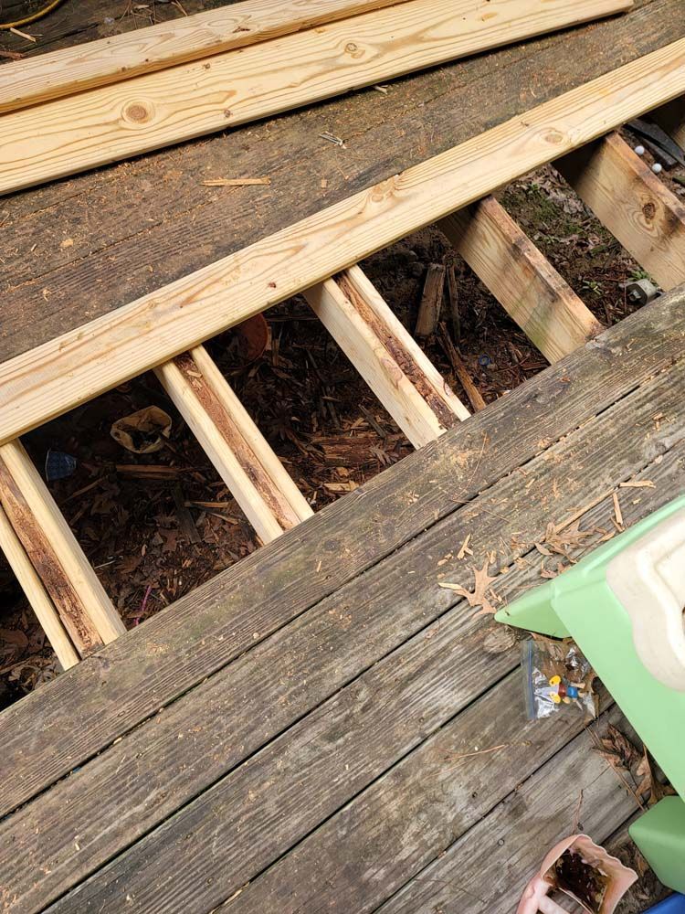 Deck planks being replaced; exposed joists and debris visible between boards, wood tones.