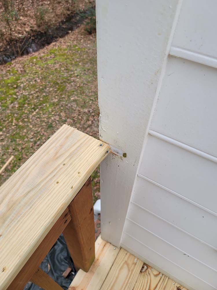 Wooden deck with handrail next to a white wall; screws visible.