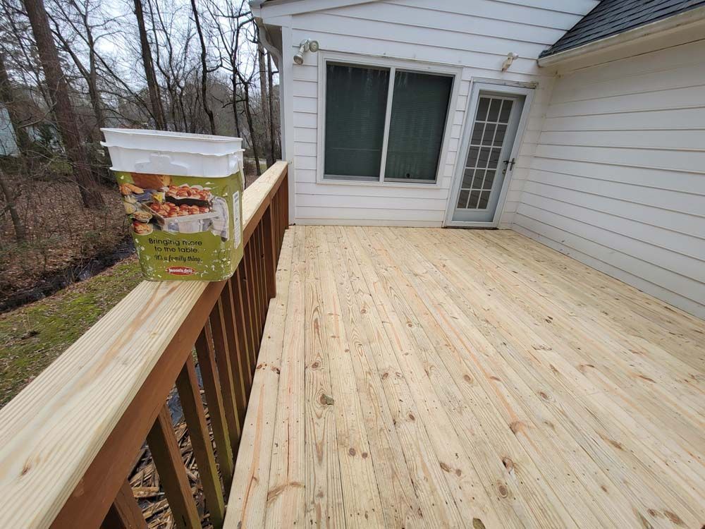 Wooden deck next to a white house, with a bucket of stain and a door.