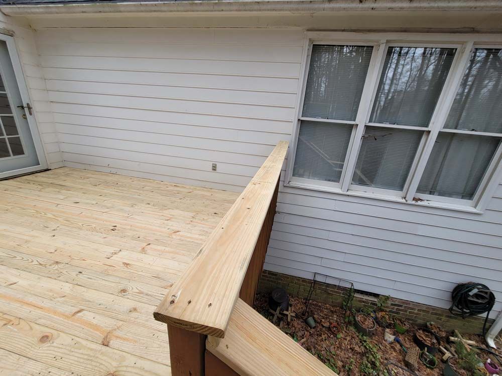 Wooden deck with railing against a white house.