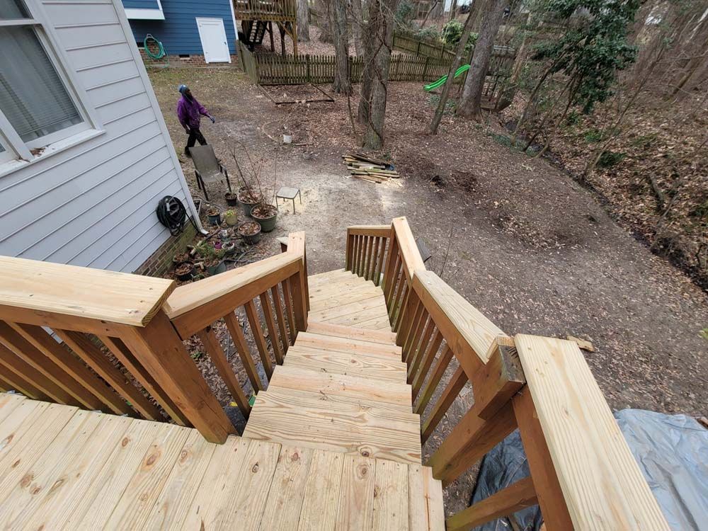 Wooden deck and stairs leading to a wooded area; person walking away; brown and green.