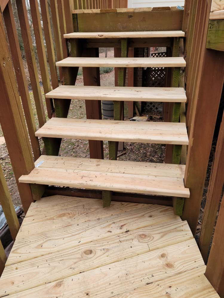 Wooden outdoor staircase leading up to a deck. The stairs have light-colored treads and green supports.