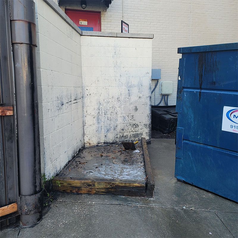 An alley with a dumpster and stained walls. Wet, concrete platform, and a rusted pipe.