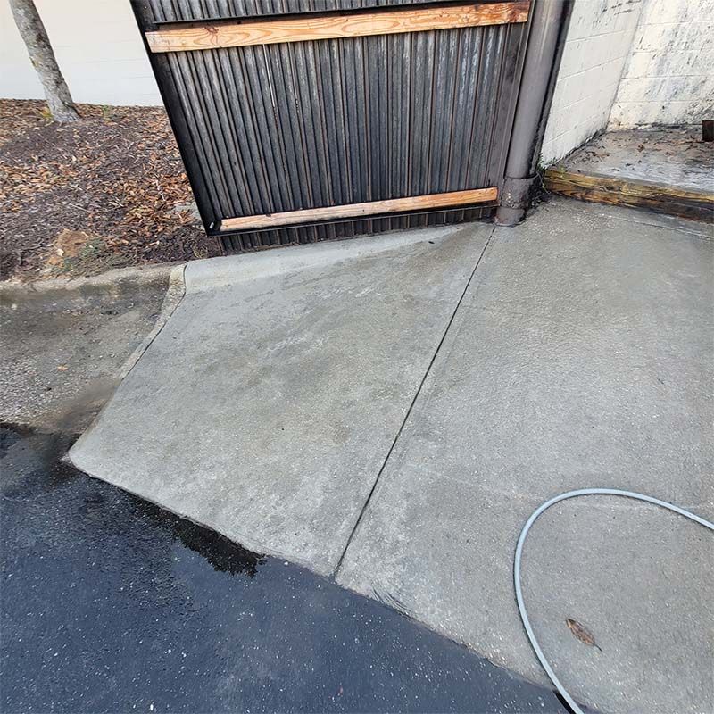 Concrete ramp leading to a metal gate. Asphalt and landscaping visible.