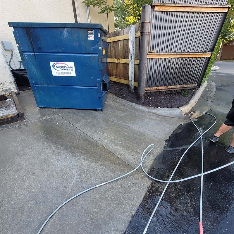 Blue dumpster next to a fence being cleaned with a hose.