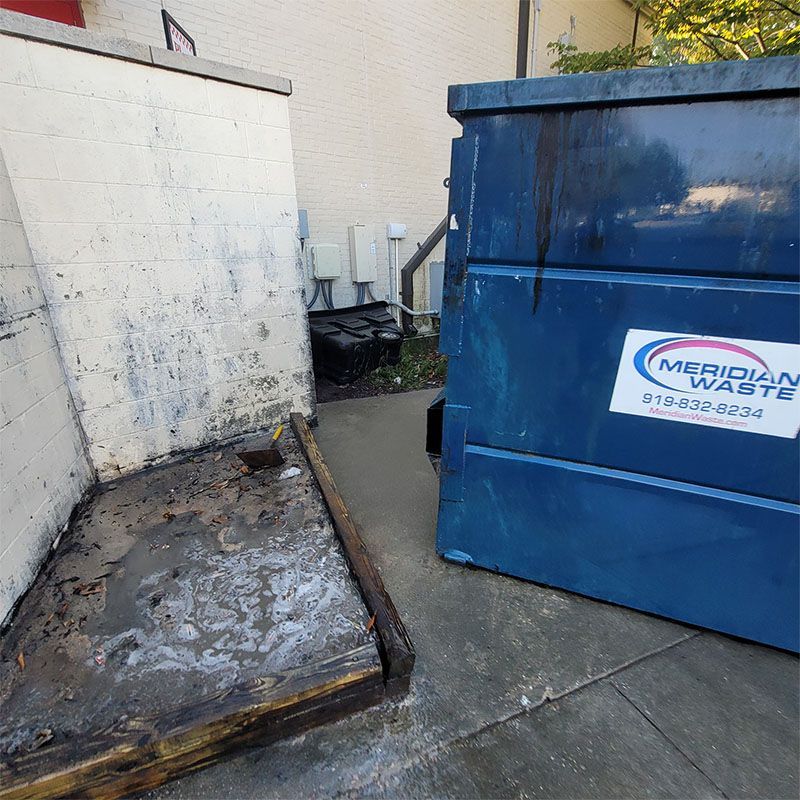 Blue dumpster next to a building with a concrete enclosure. The ground is wet.