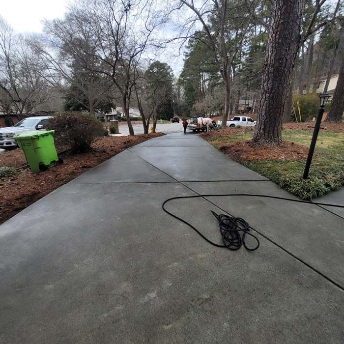 Long driveway, grey concrete, with a green trash can on the left, and two people walking in the distance.
