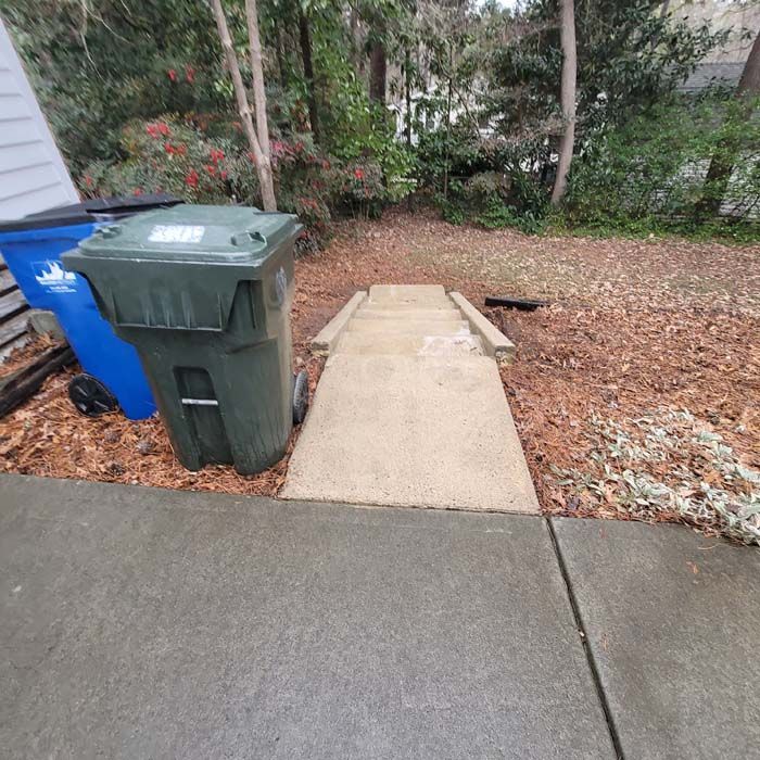 Concrete ramp and stairs leading into a backyard, with two trash cans in the foreground.