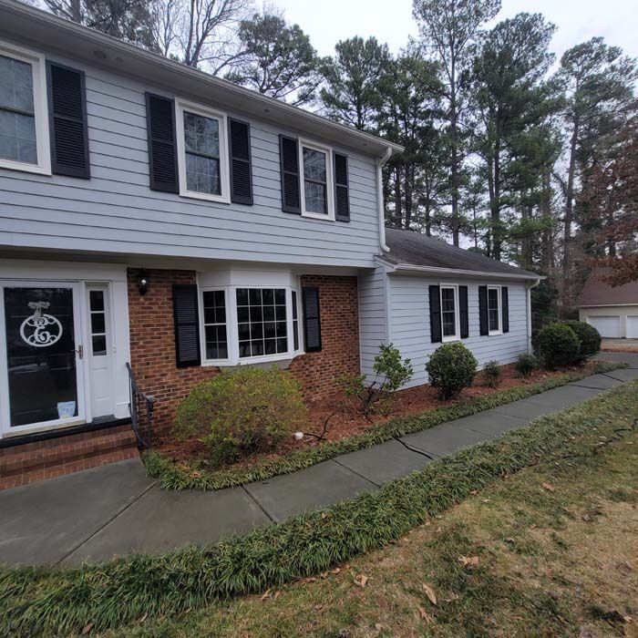 Two-story house with blue siding, brick, black shutters, and a walkway lined with green plants.