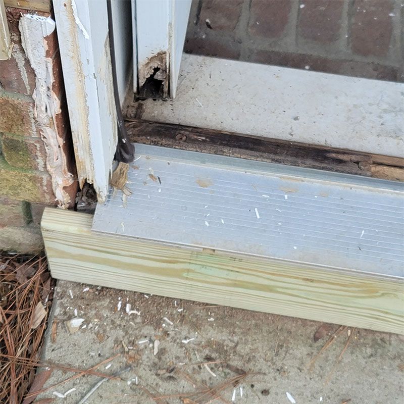 Damaged door frame with a wooden base and metal threshold.