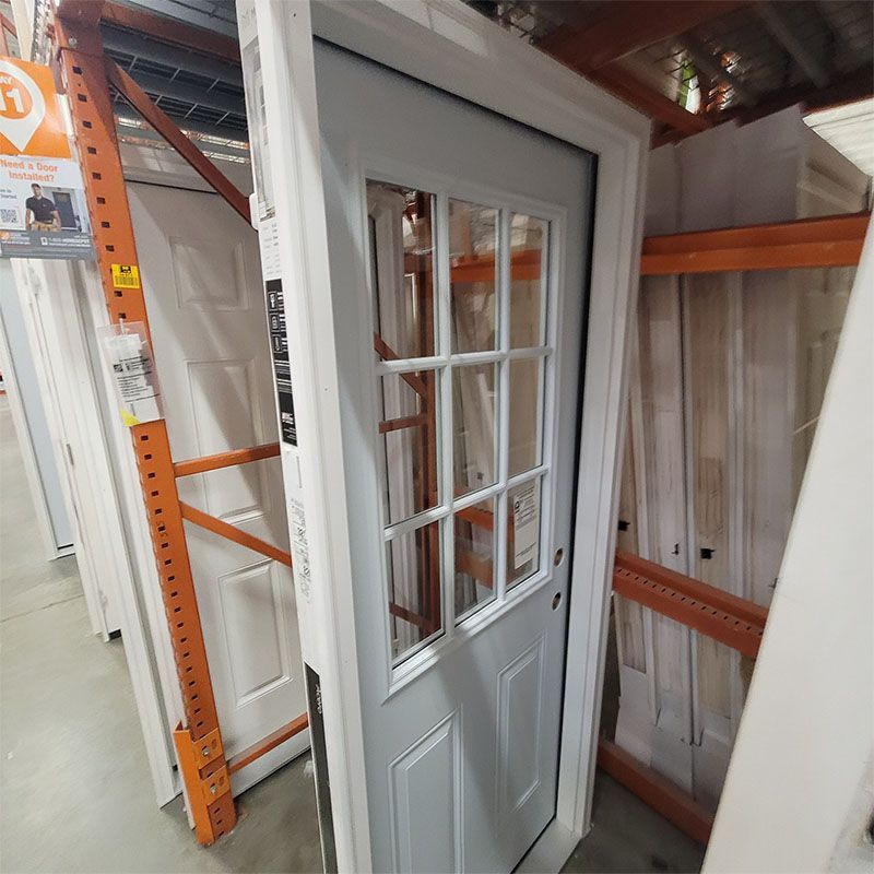 Gray door with glass panes and white trim in a store, leaning against shelves.