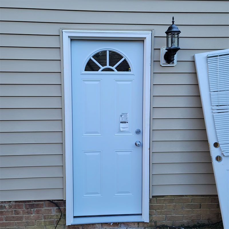 White door with arched window, on a beige-sided building. A light fixture is to the right.