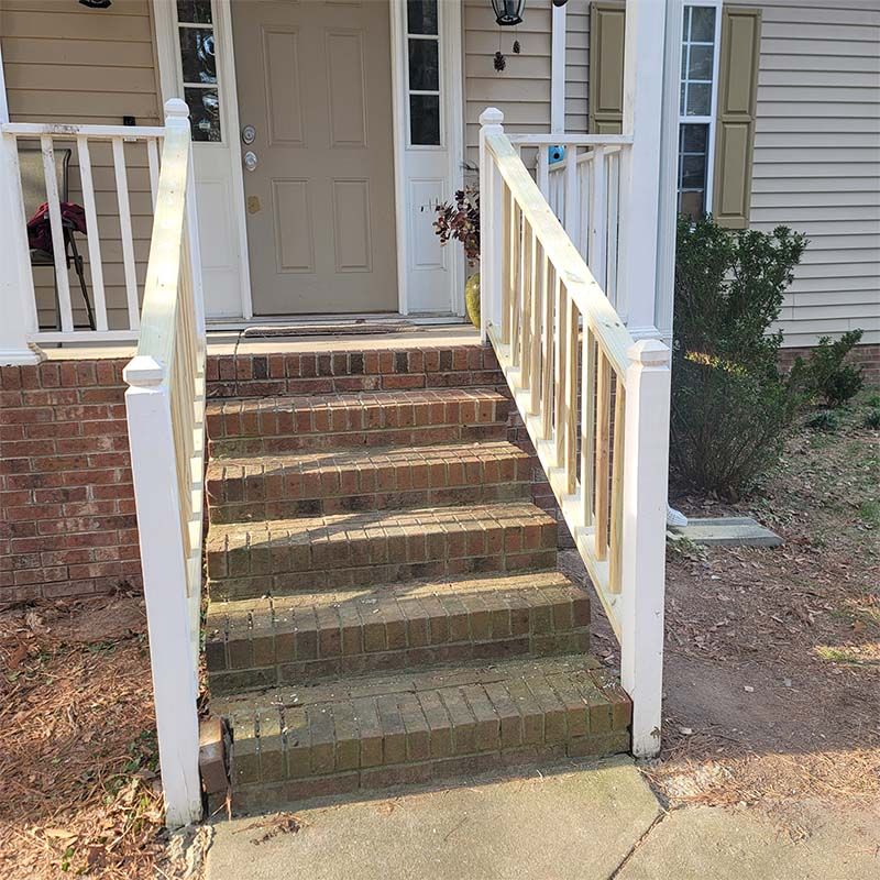 Brick steps with white railing leading to a house with a beige door.