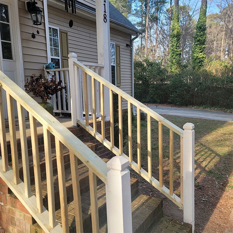 Wooden steps and railing leading to a light-colored house with a black lamp and address numbers.
