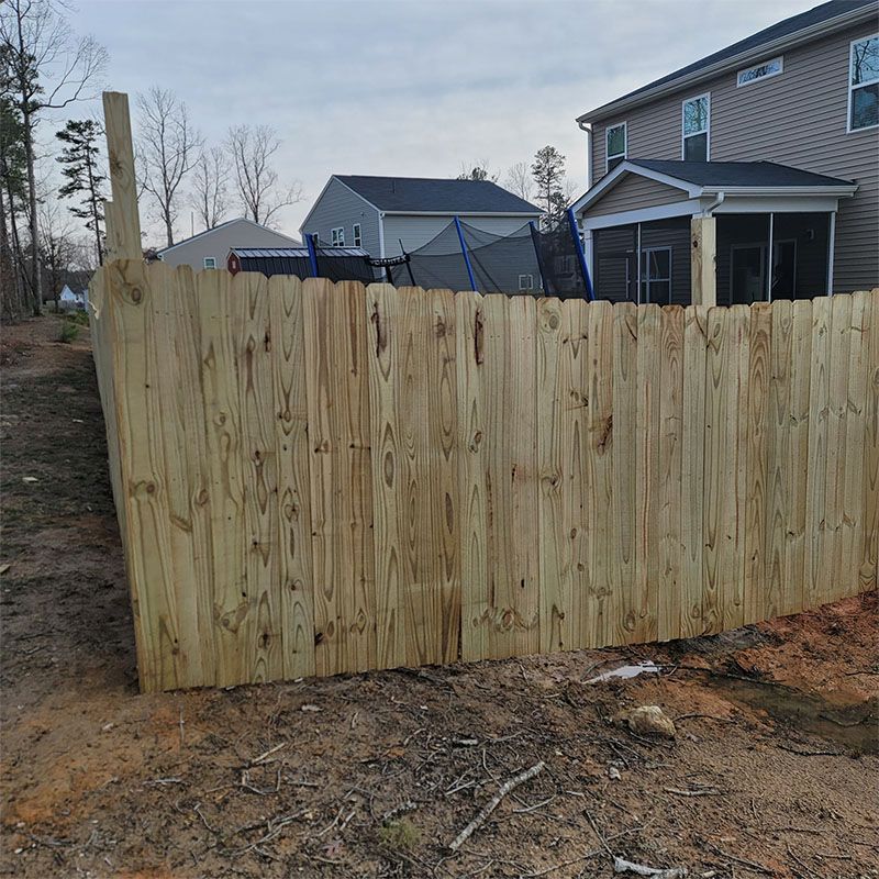 A wooden fence surrounds a backyard, with a house and trampoline visible in the background.