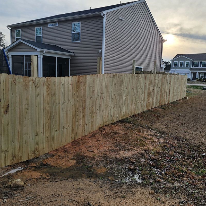 Wooden fence beside a two-story tan house and a house in the distance at dusk.