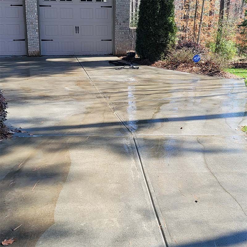 Driveway partially cleaned with a pressure washer, showing contrast in concrete color.