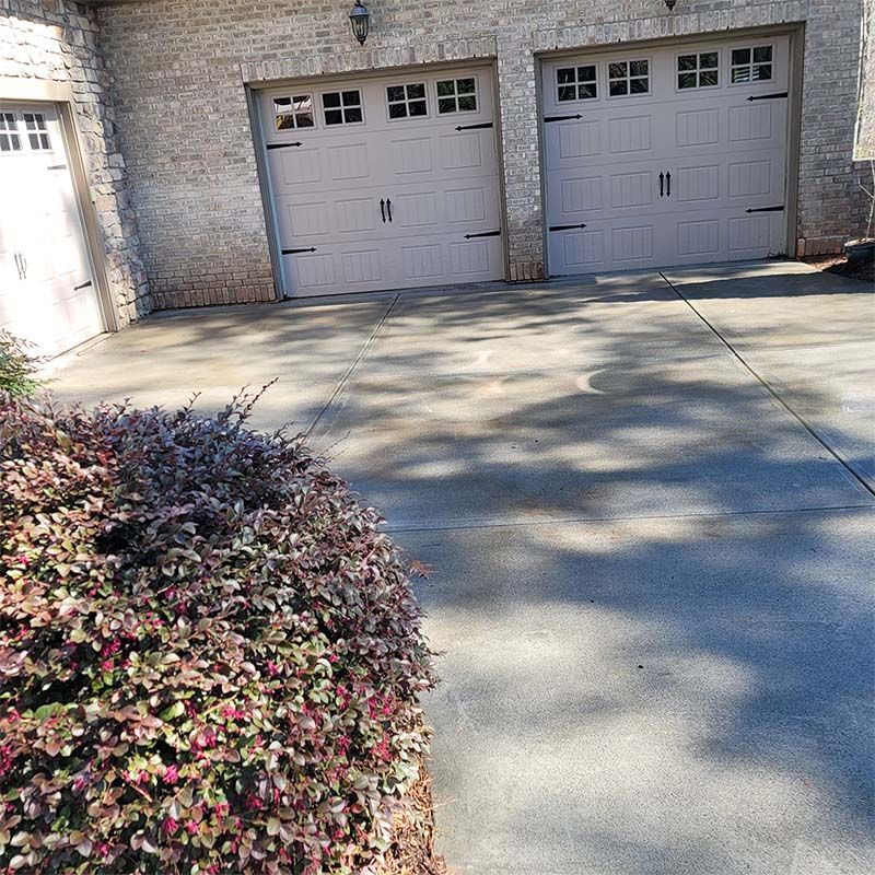 Garage with tan doors, light brick, and a shrub in the foreground.
