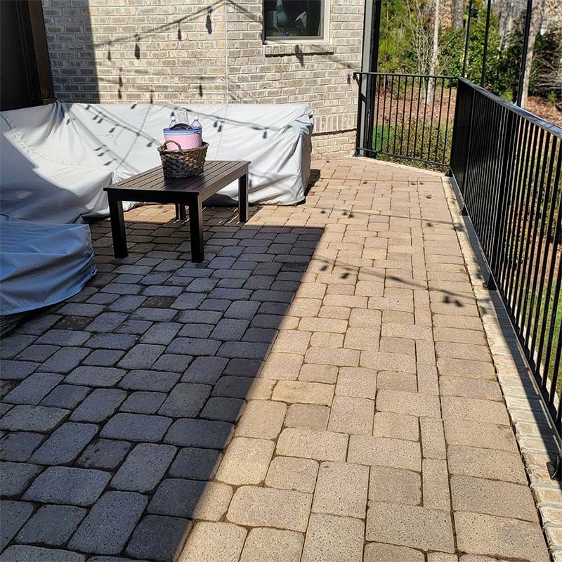 Brick patio with dark table, covered furniture, black railing, and brick wall.