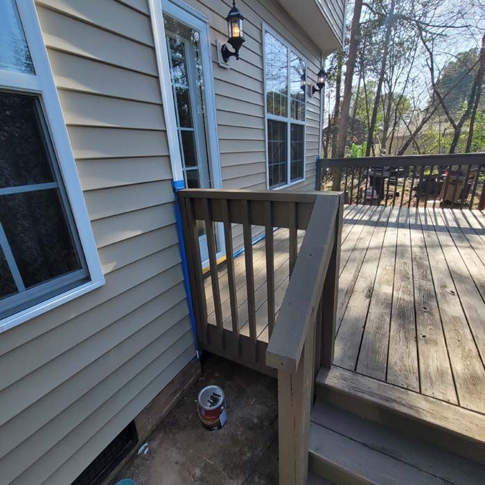 Tan siding on a house with a wooden deck, handrail, and windows. Paint can sits below the deck.
