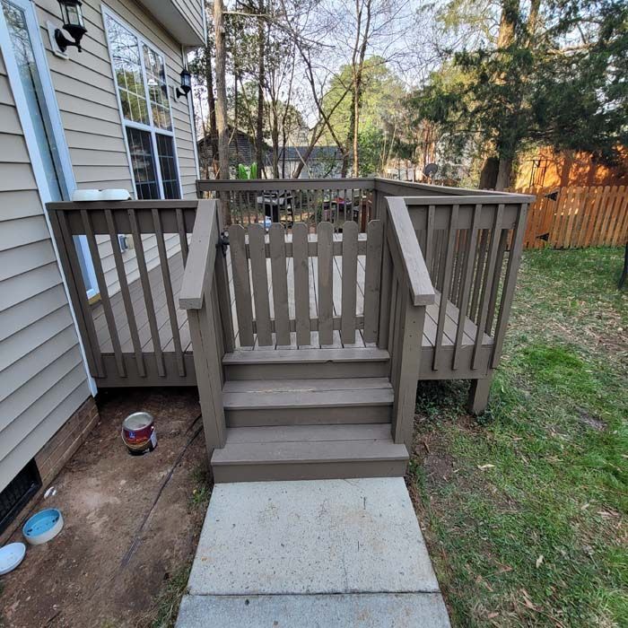 Wooden deck with steps and gate, painted brown. Concrete path in yard.