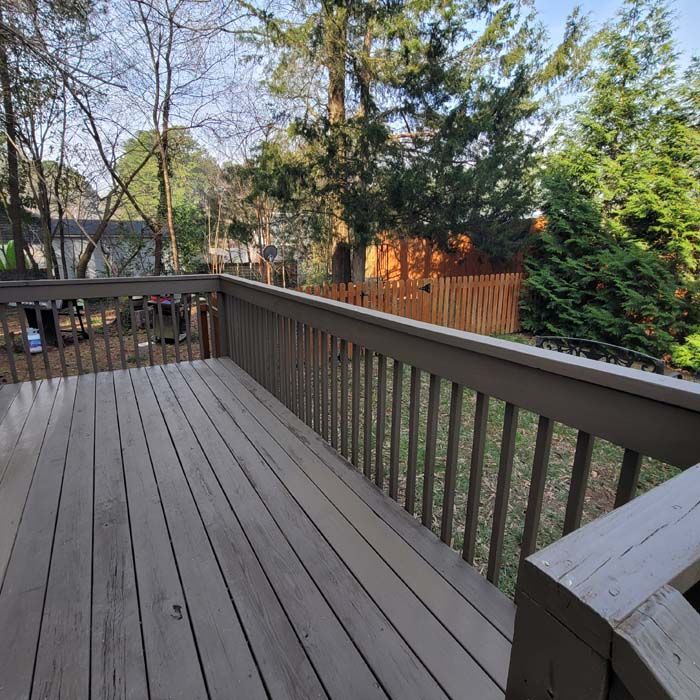 A wooden deck with a railing overlooks a backyard with trees and a fence.