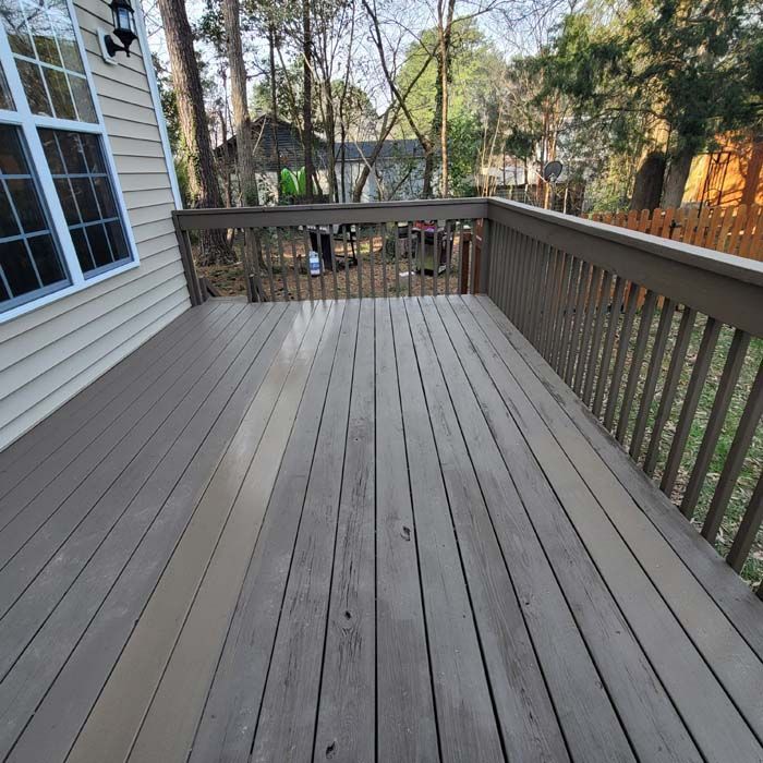 Wooden deck painted in shades of gray next to a house with a wooded backyard.