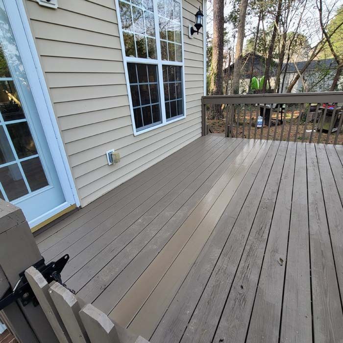 Wooden deck and house exterior. Beige siding, brown deck boards, glass windows, and a backyard view.