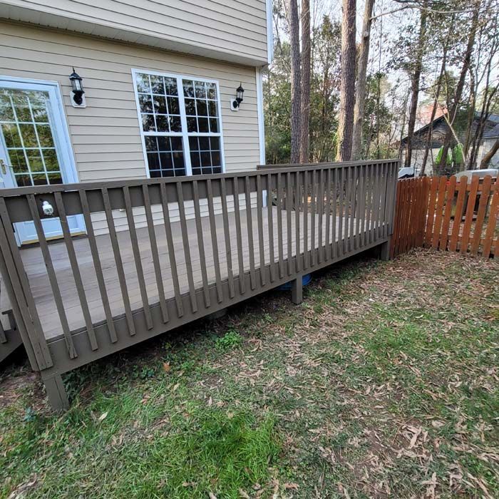 A wooden deck with railing attached to a beige house. Grass and a small fence in the yard.