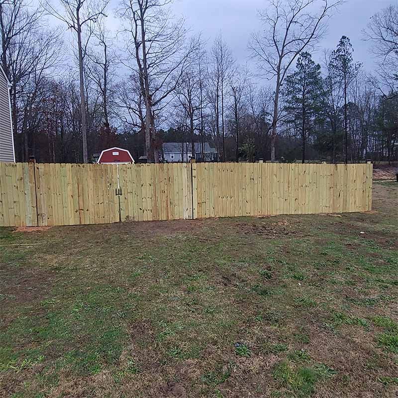 Wooden fence in backyard, with bare trees and cloudy sky.