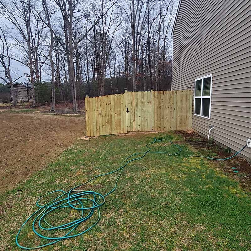 Wooden fence next to a house, with a coiled green hose in front.