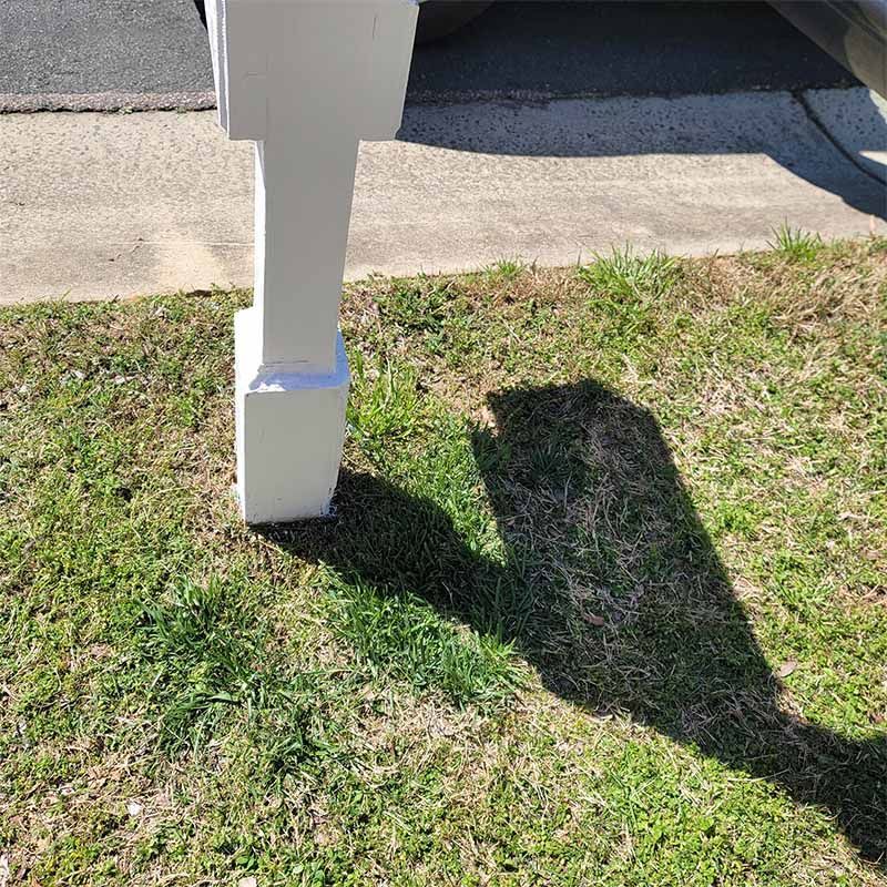 White post casting a long shadow on green grass, next to a sidewalk and curb.