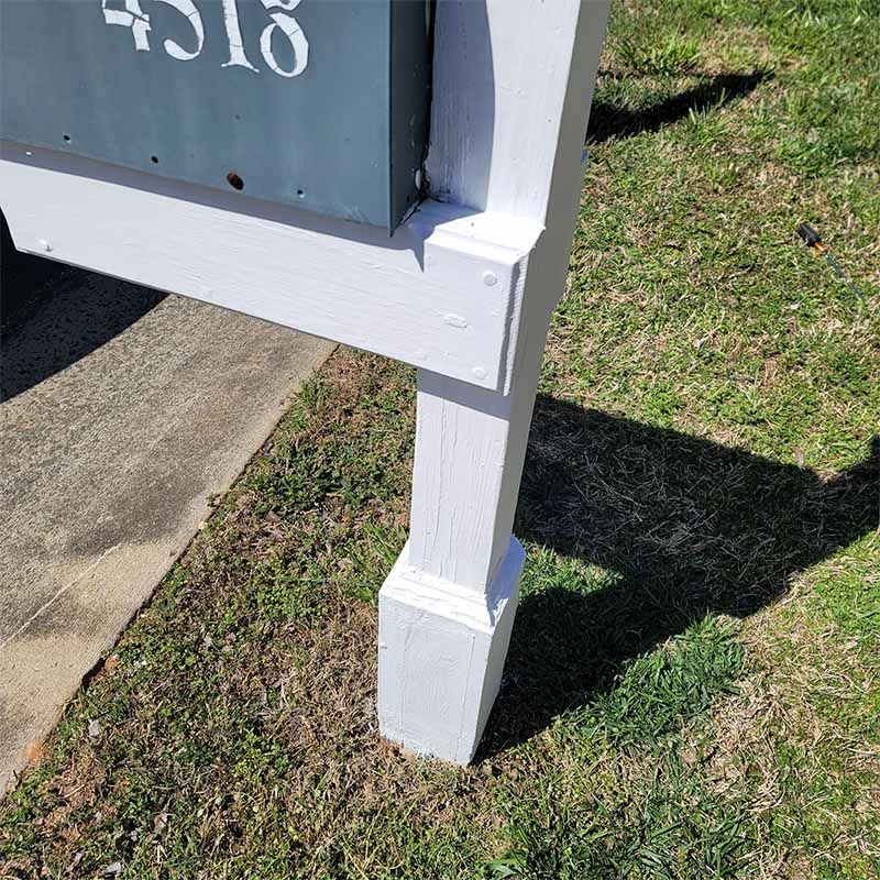 Gray painted mailbox post with address on a green lawn.