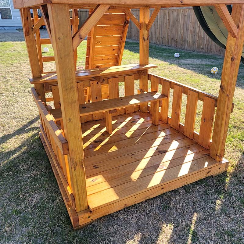 Wooden playhouse with stairs and platform in a grassy yard.