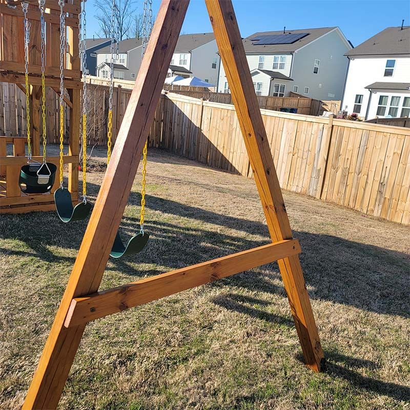 Wooden swing set in backyard, on a sunny day.