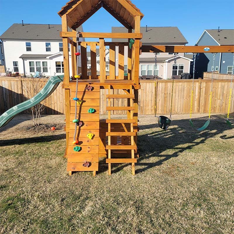 Playground set with slide, climbing wall, and ladder in a backyard.