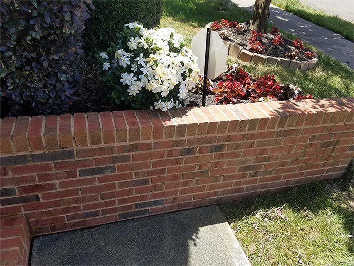 Brick retaining wall with colorful flowers in a garden bed, beside a walkway and grass.