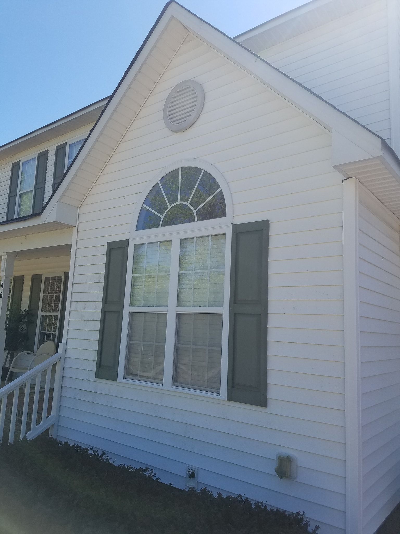 White house with green shutters and a round window under the roof peak on a sunny day.