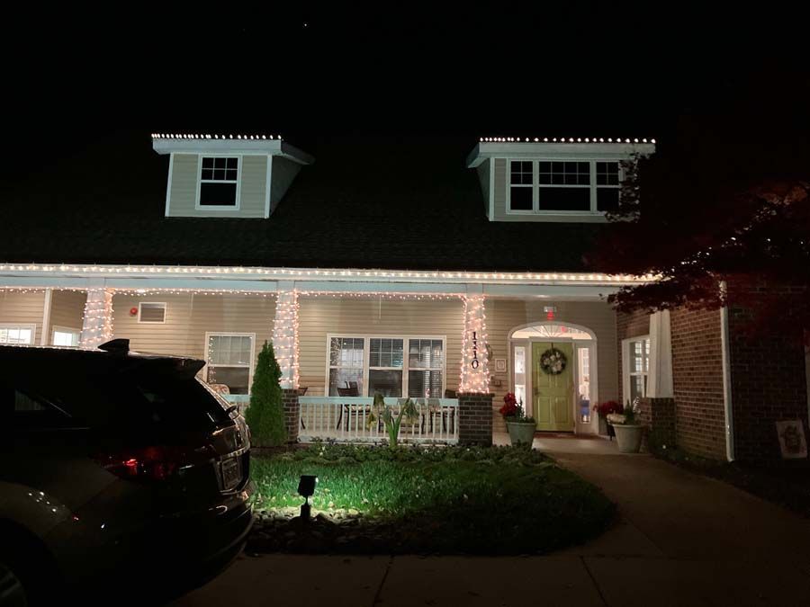 House decorated with Christmas lights at night. Front porch with wreath on door.