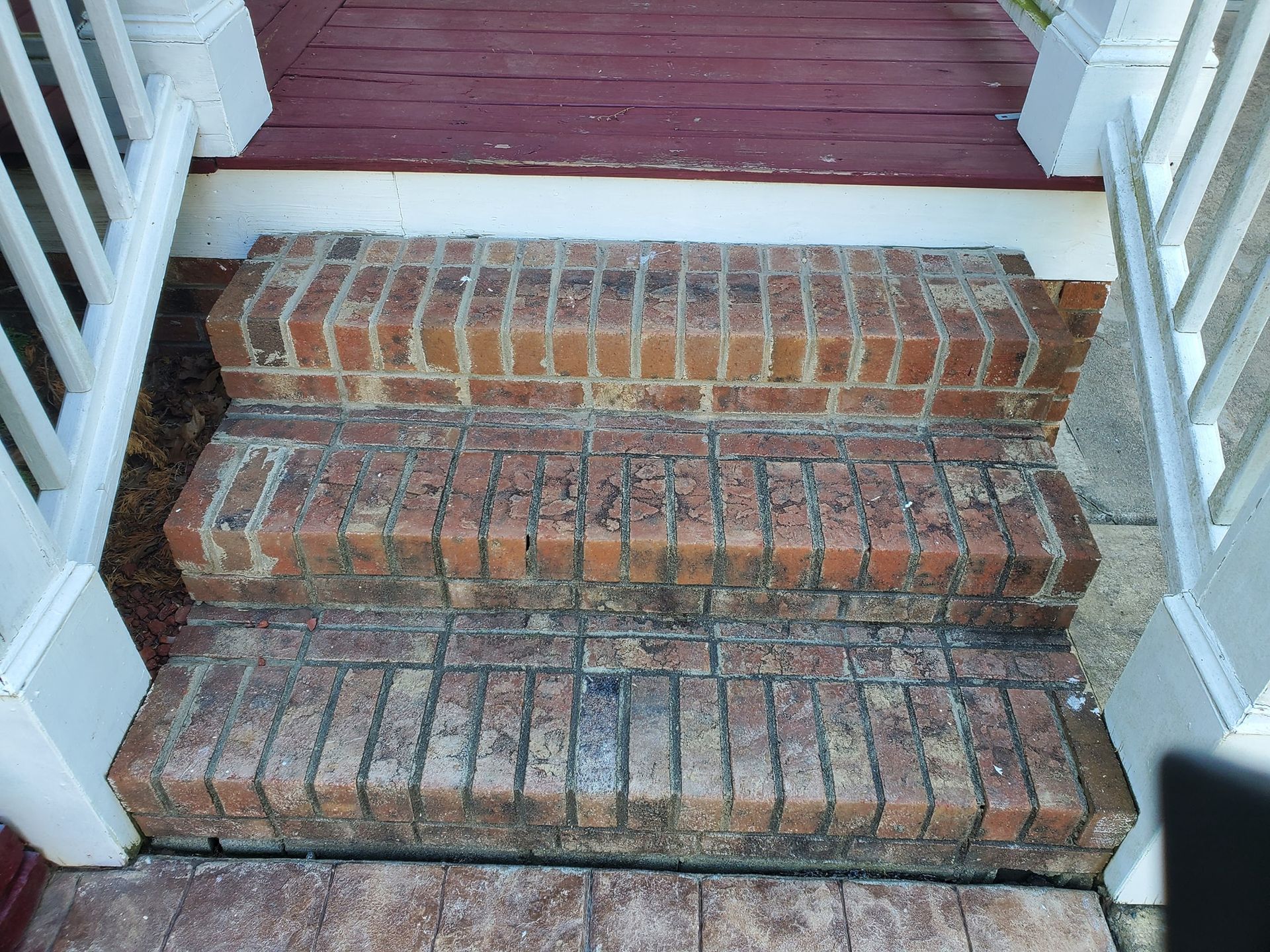 Brick steps leading up to a red porch with white railings.