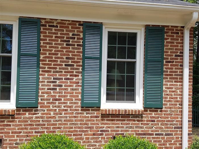 Brick house exterior with green shutters and white-framed windows.