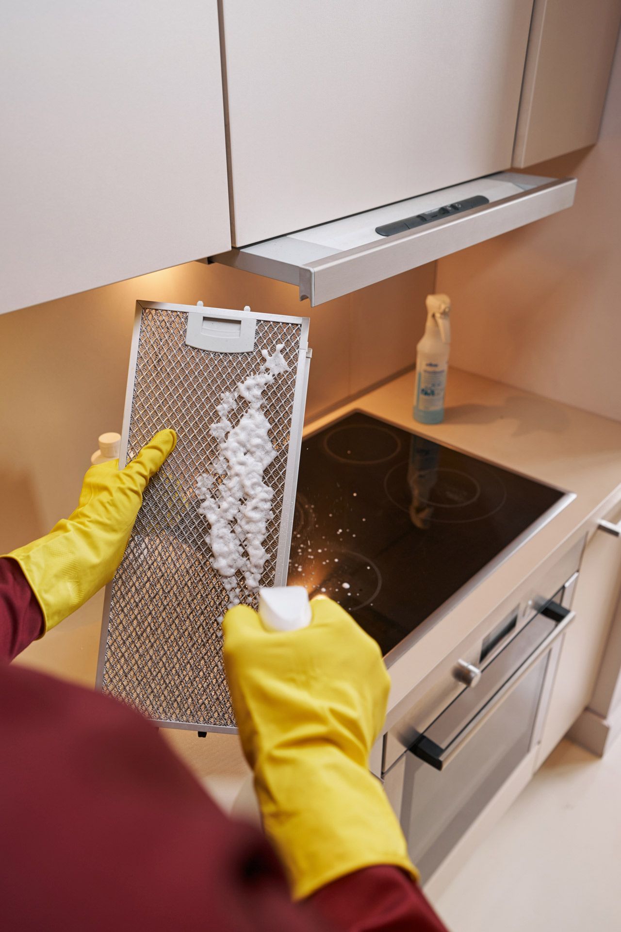 Person in yellow gloves cleaning a range hood filter above a stove in a kitchen.