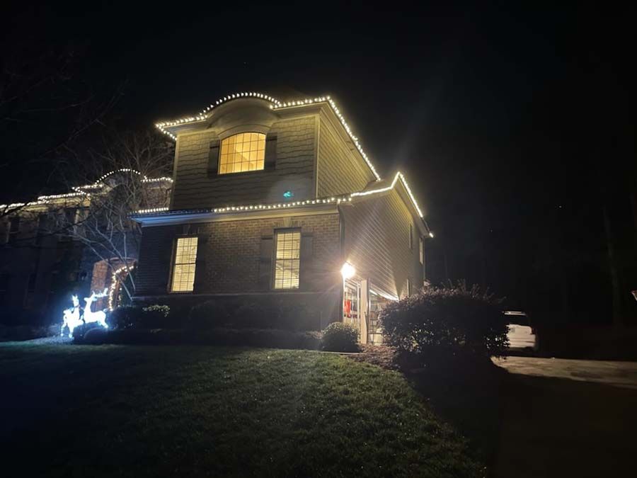 Two-story house lit with white Christmas lights at night.